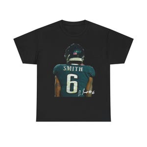 Puede incluir: Camiseta negra con un diseño de camiseta de fútbol verde azulado. La camiseta muestra el nombre "SMITH" y el número "6" en blanco. El jugador lleva un casco. Una firma es visible debajo del número.