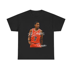 Puede incluir: Camiseta negra con un retrato de Rob Dillingham con una camiseta de baloncesto roja con el número 7. El nombre del jugador y "Rebuildshifts" están escritos en blanco. La camiseta tiene un cuello redondo clásico.