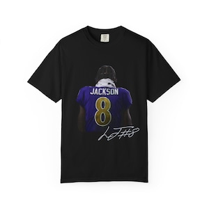 May include: Black t-shirt featuring a graphic of a football player in a purple jersey with the number 8 and the name "Jackson". The player is seen from the back. A signature is below the graphic.