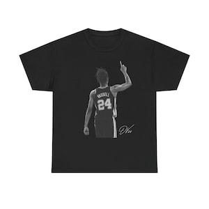 Pode incluir: Uma t-shirt preta de manga curta com um gráfico monocromático de um jogador de basquetebol visto de costas. O jogador veste uma camisola com o nome VASSELL e o número 24. O jogador tem um braço levantado e a assinatura DV24 está abaixo.