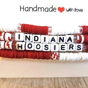 May include: Stack of four handmade bracelets. The bracelets are white and red, with the words "INDIANA HOOSIERS" spelled out in white letter beads. The top of the display card reads "Handmade with love."