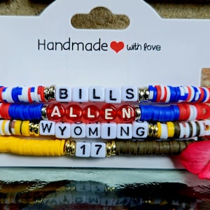 May include: Handmade beaded bracelets with the words "BILLS", "ALLEN", "WYOMING", and "17". The bracelets are in red, white, blue, yellow, and brown. The top bracelet has red, white, and blue beads. The second bracelet has blue and red beads. The third bracelet has yellow and white beads.