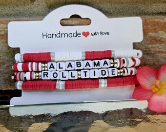 May include: A stack of handmade bracelets in red, white, and silver. The bracelets spell out "ALABAMA ROLL TIDE" using white letter beads. The card reads "Handmade with love" with a heart symbol.