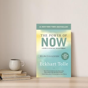 May include: A teal blue book cover with the title "The Power of Now" in white text. The subtitle is "A Guide to Spiritual Enlightenment" in smaller white text. The author's name, "Eckhart Tolle", is in white text on a teal blue background. The book cover also features a gold starburst with the text "Over 15 Million Copies Sold" in white text.