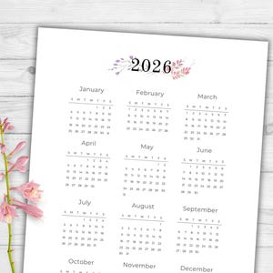 May include: A printed 2026 calendar with a floral design at the top. The calendar is white with black text, displaying the months from January to December. The days of the week are abbreviated, and the dates are clearly visible.