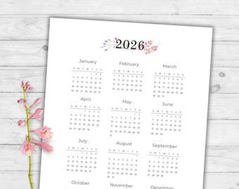 May include: A printed 2026 calendar with a floral design at the top. The calendar is white with black text, displaying the months from January to December. The days of the week are abbreviated, and the dates are clearly visible.