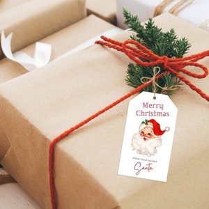 May include: A brown gift box with a red ribbon and a white gift tag. The gift tag has a vintage illustration of Santa Claus and the text "Merry Christmas" and "From your Secret Santa".