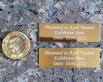 May include: Two gold plaques with engraved text. The text reads "Presented to Ayub Mumin Exhibition Bout Date: 10.04.2022".