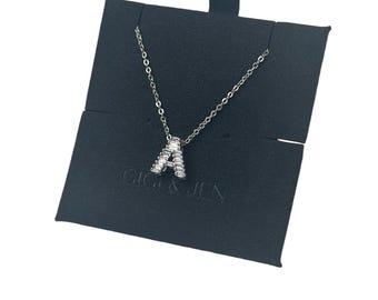Può includere: Una collana d'argento con un ciondolo a forma di lettera A incrostato di cristalli trasparenti a forma di baguette. La collana è esposta in un cofanetto per gioielli in velluto nero con il testo "Gigi & Jen" stampato sul davanti.