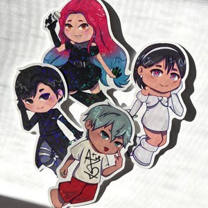 Op de afbeelding: Een verzameling van vijf stickers in anime-stijl. De personages hebben verschillende kapsels, outfits en poses. Eén personage houdt een microfoon vast, een ander draagt een shirt met een grafisch ontwerp. De stickers hebben een witte rand.