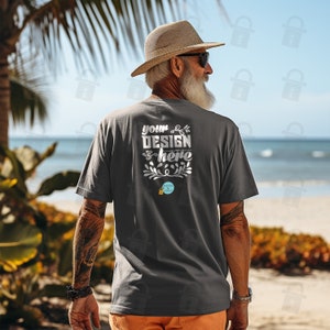 Könnte beinhalten: Ein dunkelgraues T-Shirt mit dem Text "your design here" und einem kleinen Blumenmuster. Das Shirt wird von einer Person am Strand getragen.