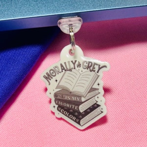 May include: A white charm with a stack of books and the text "Morally Grey is my favorite color".
