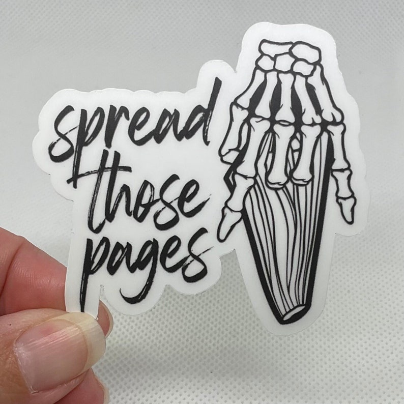 Puede incluir: Una pegatina blanca con texto negro y una ilustraci&oacute;n de una mano esquel&eacute;tica. El texto dice "spread those pages" en un estilo manuscrito. La mano esquel&eacute;tica sostiene una pila de p&aacute;ginas.