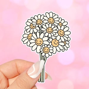 以下が含まれることがあります： 白いデイジーの花束のステッカー。各花の中心に黄色い笑顔があります。デイジーは円形に配置され、茎は中央から下に伸びています。