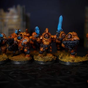 May include: A group of miniature figurines in orange armor, some with blue accents, and weapons. One figure holds a blue sword. The figurines stand on a textured, yellow-brown base. The date "01 20 2026" is visible in the bottom right corner.