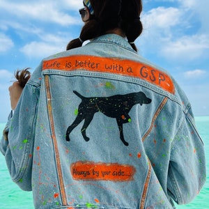 May include: A blue denim jacket with paint splatters and the text "Life is better with a GSP Always by your side..." in orange. A black silhouette of a dog is painted on the back.
