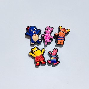 May include: Five colorful cartoon character shoe charms. The charms feature characters in blue, pink, orange, yellow, and red. The charms are made of a rubbery material and are designed to be attached to shoes.