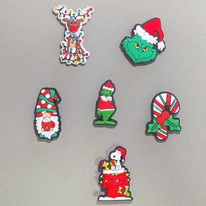 May include: A set of six Christmas-themed magnets featuring a reindeer with lights, the Grinch, a gnome, a candy cane, a snowman, and a dog. The magnets are made of rubber and have a festive red, green, and white colour scheme.