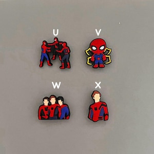 May include: Four different charms featuring Spider-Man characters. The first charm shows three Spider-Man figures in a fighting pose. The second charm shows a single Spider-Man figure with a web design. The third charm shows three Spider-Man figures standing together. The fourth charm shows a single Spider-Man figure standing with his arms crossed.