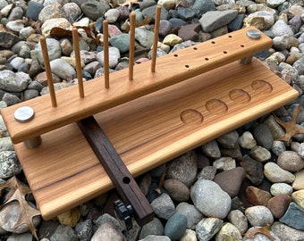 May include: Wooden organizer with multiple slots for holding tools or other items. The organizer has a dark brown wood base and a lighter brown wood top with a row of holes and a row of slots. The organizer is sitting on a bed of small rocks.