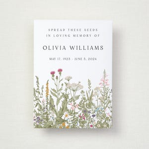 May include: A white card with the text "SPREAD THESE SEEDS IN LOVING MEMORY OF OLIVIA WILLIAMS" and dates "MAY 17, 1923 - JUNE 5, 2024." The bottom of the card features a colourful illustration of wildflowers.