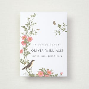 May include: A white memorial card featuring the text "IN LOVING MEMORY" and the name "OLIVIA WILLIAMS" with dates. The card is adorned with pink roses, green foliage, a bird, and a butterfly.