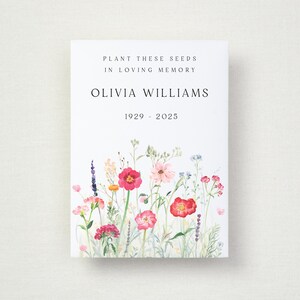 May include: A white rectangular card featuring a watercolor illustration of colorful wildflowers at the bottom. The text reads: PLANT THESE SEEDS IN LOVING MEMORY, OLIVIA WILLIAMS, 1929 - 2025. The design uses a clean, centered layout with black serif typography.