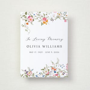 May include: A white memorial card with floral decoration. The card reads "In Loving Memory" above the name "OLIVIA WILLIAMS" and the dates "MAY 17, 1923 - JUNE 5, 2024". The corners are adorned with colourful flowers and foliage.