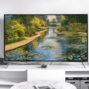 May include: A large flat-screen television displays a vibrant landscape painting of a pond with lily pads and a walking path. The TV is on a white cabinet with a black metal shelf and a small side table.