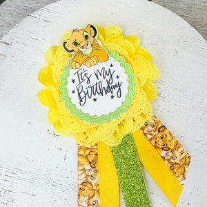 Puede incluir: Un botón de cumpleaños amarillo y verde con un cachorro de león de dibujos animados y el texto "It's my Birthday".