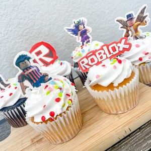 Puede incluir: Seis cupcakes decorados con chispas de colores y adornos con tem&aacute;tica de Roblox. Los adornos incluyen un logotipo de Roblox rojo, un personaje de Roblox con una camisa a rayas rojas y blancas, un personaje de Roblox con cabello morado y un personaje de Roblox con una camisa amarilla y un sombrero.