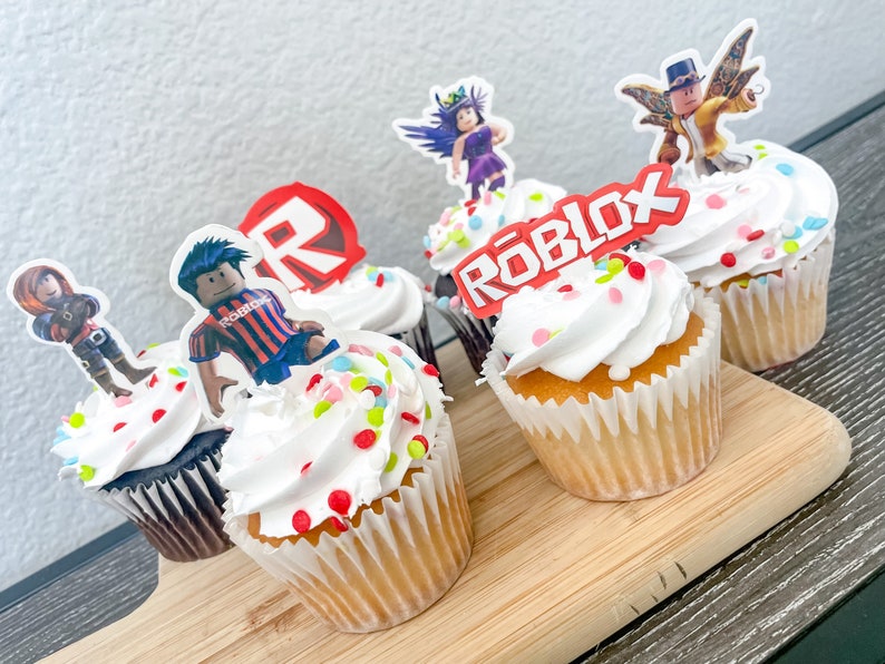 Puede incluir: Seis cupcakes decorados con chispas de colores y adornos con tem&aacute;tica de Roblox. Los adornos incluyen un logotipo de Roblox rojo, un personaje de Roblox con una camisa a rayas rojas y blancas, un personaje de Roblox con cabello morado y un personaje de Roblox con una camisa amarilla y un sombrero.