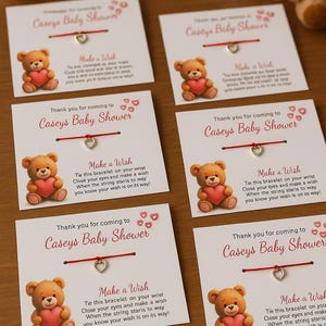 May include: Baby shower favors featuring a teddy bear holding a heart. Each card reads "Thank you for coming to Casey's Baby Shower" and includes a "Make a Wish" bracelet with a heart charm and red string.