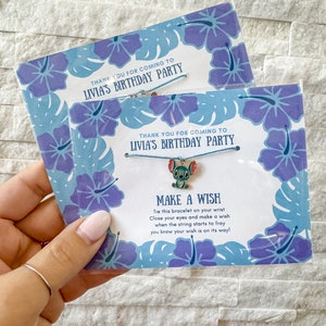 May include: Blue and white birthday party favor with a blue string bracelet and a small blue Stitch charm. The card says "Thank you for coming to Livia's Birthday Party" and "Make a Wish". Tie this bracelet on your wrist, close your eyes and make a wish. When the string starts to fray, you know your wish is on its way!"