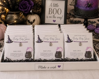 Könnte beinhalten: Ein Set aus violetten Schnurarmbändern mit silbernen Anhängern, verpackt auf Karten mit der Aufschrift 'Thank you for coming to Beckys Baby Shower' und 'Make a wish', inklusive einer Illustration von Hexenhut und Kessel.
