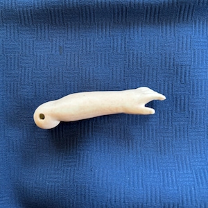 May include: A small, off-white, carved bone pendant shaped like an arm with a hole at the top for a cord.