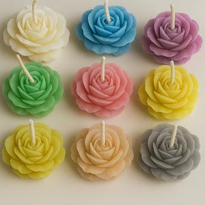 K&ouml;nnte beinhalten: Eine Sammlung von neun rosenf&ouml;rmigen Kerzen, die in einem Raster angeordnet sind. Jede Kerze hat geschichtete Bl&uuml;tenbl&auml;tter in verschiedenen Farben wie Creme, Blau, Lila, Gr&uuml;n, Rosa, Gelb, Hellgelb, Pfirsich und Grau mit einem wei&szlig;en Docht.