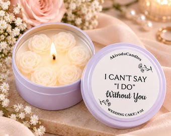 May include: A light purple round metal candle tin containing a soy wax candle with six small white rose-shaped wax embeds and a lit wick. The lid features the text AkivoduCandles, I CAN'T SAY "I DO" Without You, WEDDING CAKE, and 4 OZ.