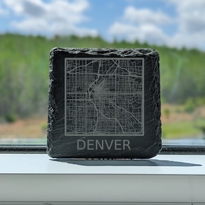 May include: A black slate coaster with a gray engraved map of Denver, Colorado. The word "DENVER" is engraved below the map.