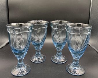 Può includere: Quattro bicchieri a stelo azzurri con un design testurizzato e a spirale. I bicchieri hanno una coppa arrotondata e un gambo corto, adatti per servire bevande. I bicchieri sono in vetro e sono disposti su una superficie scura.