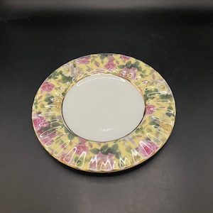 Może przedstawiać: Okrągły, dekoracyjny talerz z żółtym tłem i kwiatowym wzorem różowych i białych róż. Środek talerza jest biały, a obrzeże zdobione złotem. Talerz jest prawdopodobnie wykonany z porcelany.