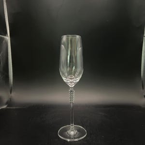 May include: A clear champagne flute with a long stem and a twisted design. The glass has a wide bowl and a round base. The background is black.