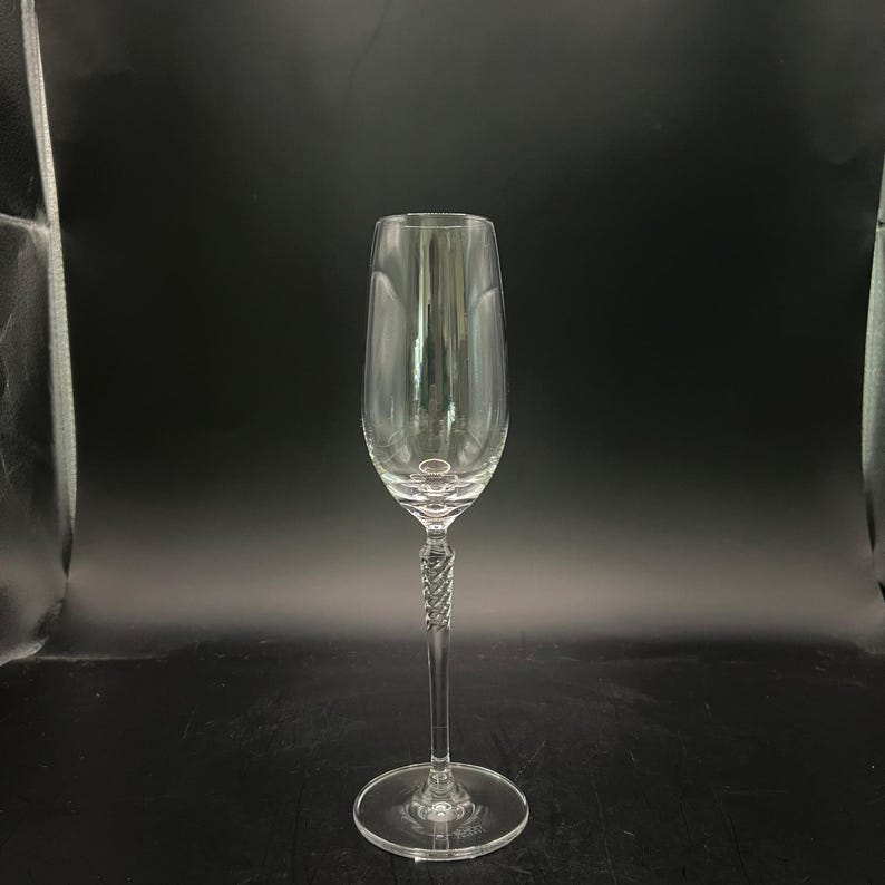 May include: A clear champagne flute with a long stem and a twisted design. The glass has a wide bowl and a round base. The background is black.