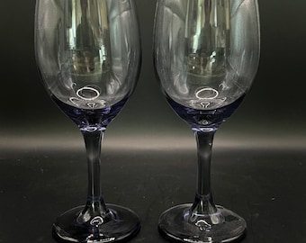 Op de afbeelding: Twee elegante wijnglazen met een heldere kelk en een donkerblauwe steel en voet. De glazen zijn leeg en reflecteren de omgeving. De steel en voet hebben een donkerblauwe tint.