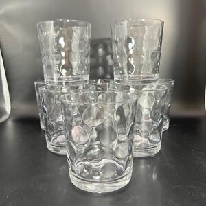 May include: Six clear glass tumblers with a textured, bubble-like design. The glasses are stacked in a pyramid shape.