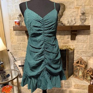 May include: A green polka dot dress with a ruffled hem and spaghetti straps. The dress is cinched at the waist and has a relaxed fit.
