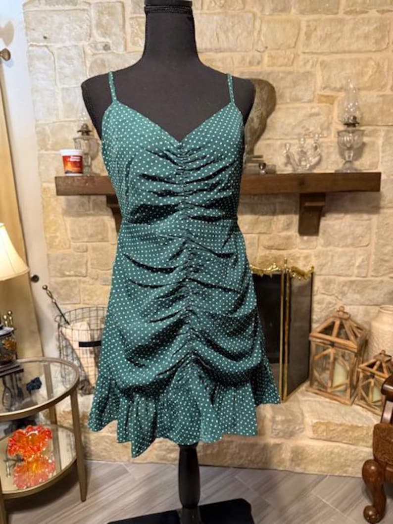 May include: A green polka dot dress with a ruffled hem and spaghetti straps. The dress is cinched at the waist and has a relaxed fit.