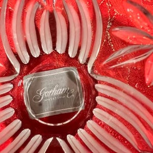Puede incluir: Un primer plano de un cuenco de vidrio transparente con un dise&ntilde;o floral rojo. El cuenco tiene un borde blanco esmerilado y una etiqueta de Gorham & Co. en la parte inferior.