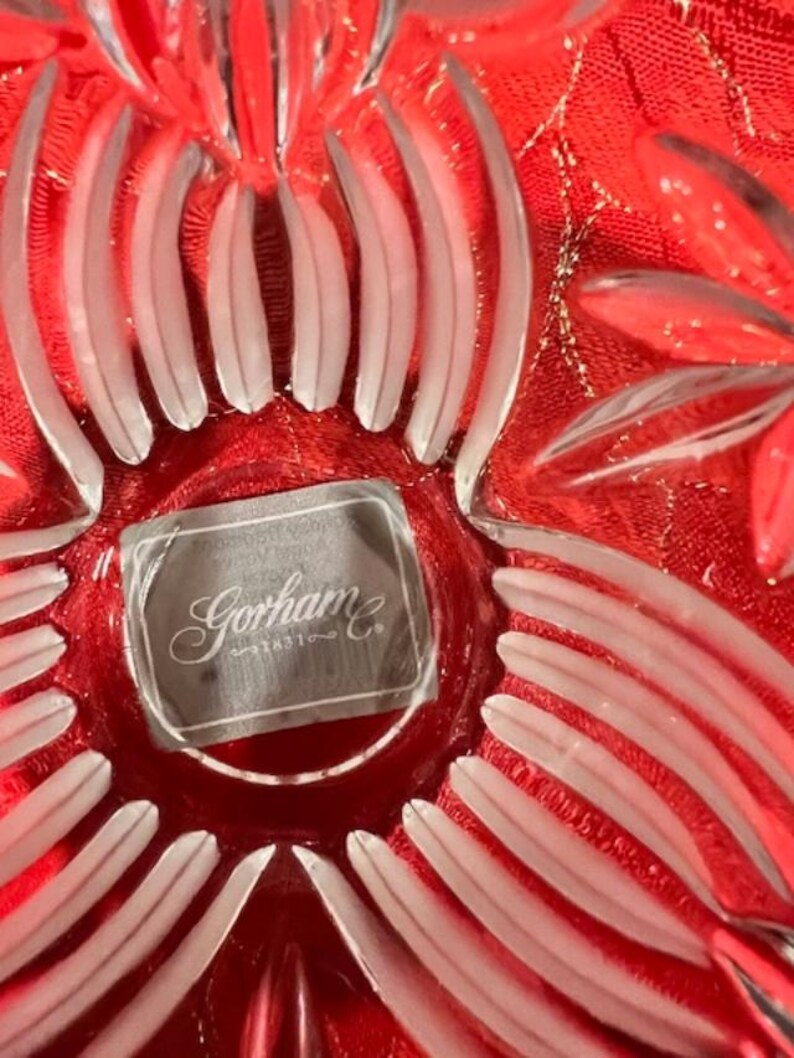 Puede incluir: Un primer plano de un cuenco de vidrio transparente con un dise&ntilde;o floral rojo. El cuenco tiene un borde blanco esmerilado y una etiqueta de Gorham & Co. en la parte inferior.