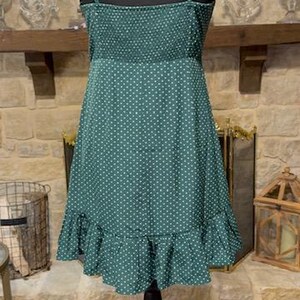 May include: A green polka dot dress with a ruffled hem. The dress has thin straps and a fitted bodice.